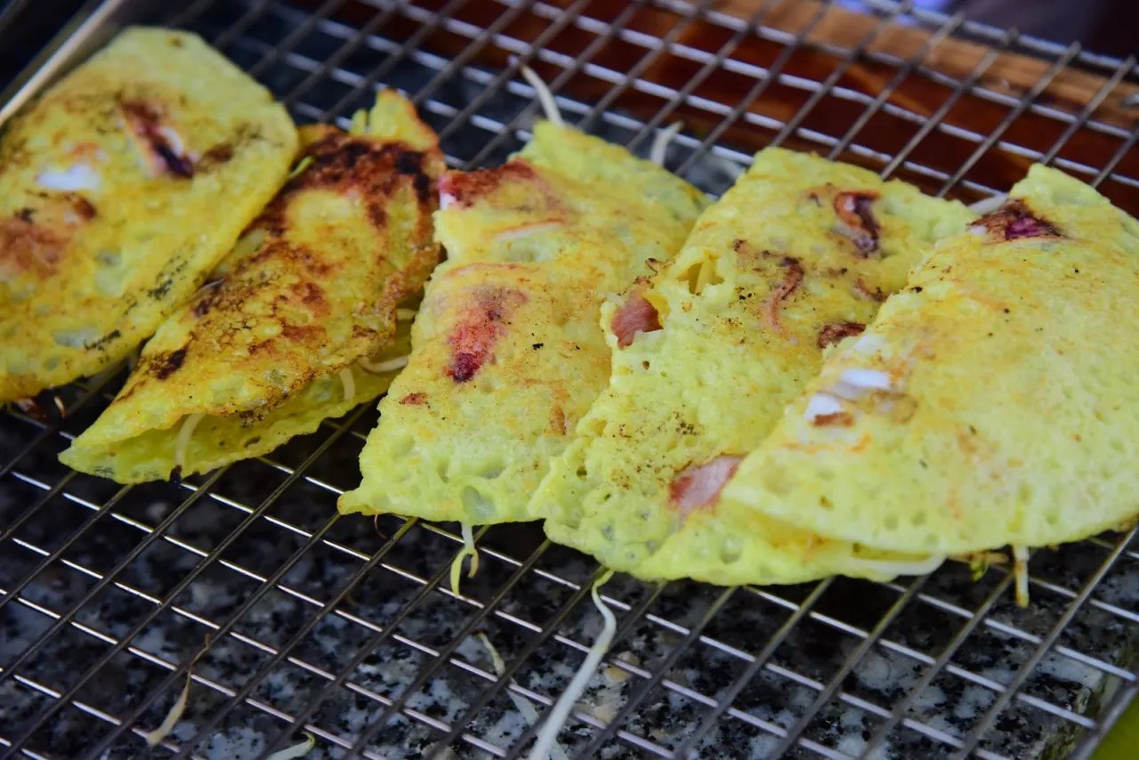 Bánh xèo vàng ươm đang chiên giòn trên vỉ, nhân tôm thịt lộ rõ