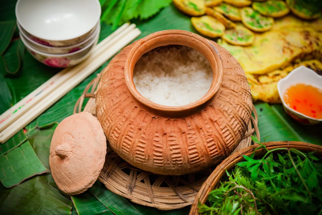 Nồi đất đựng cơm niêu bên cạnh bánh xèo và chén nước chấm, bàn ăn lá chuối