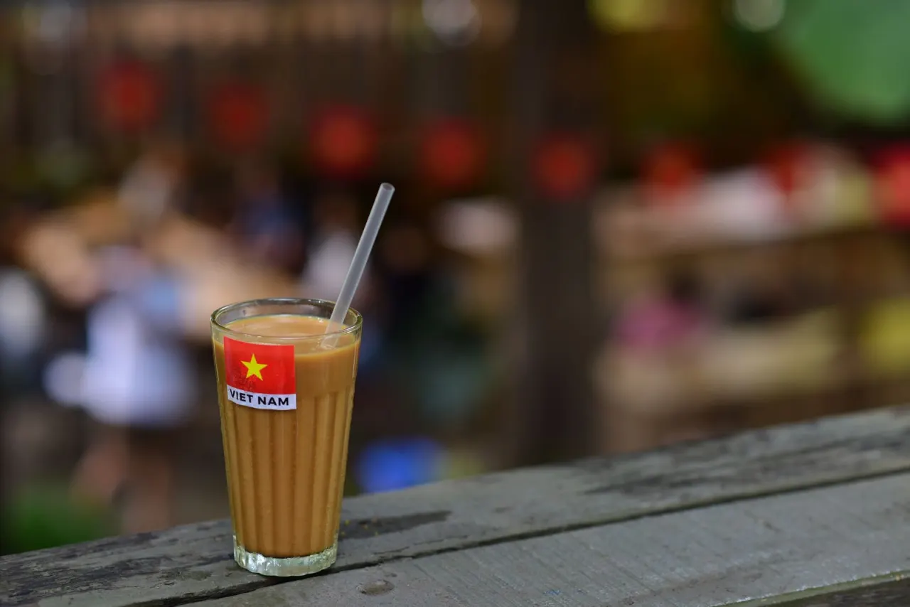 Ly cà phê sữa đá Việt Nam trên bàn gỗ, phía sau là dãy đèn lồng đỏ